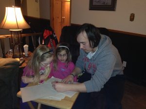 A player helping two young girls with homework at his billet home in 2015.
