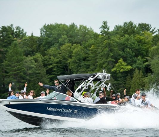 A group of participants during the Boat Rally for Kids in 2019. Attendees are cheering and waving from a moving boat with water splashing up around them.