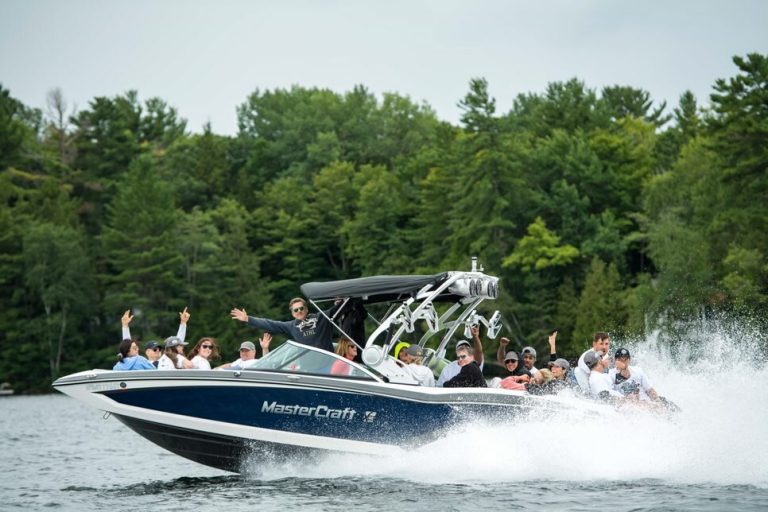 A group of participants during the Boat Rally for Kids in 2019. Attendees are cheering and waving from a moving boat with water splashing up around them.