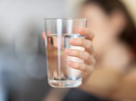 Drinking water: A woman holds out a glass of water against a blurred background