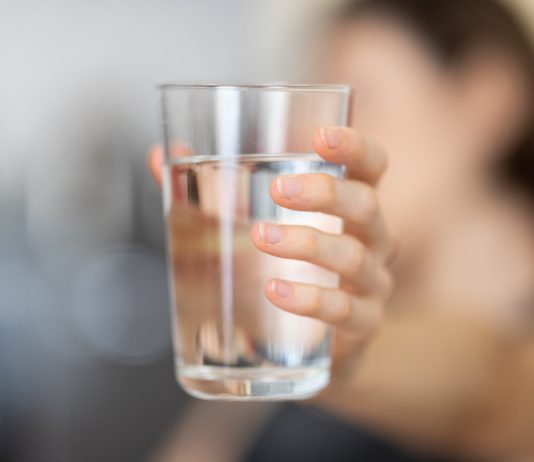 Drinking water: A woman holds out a glass of water against a blurred background