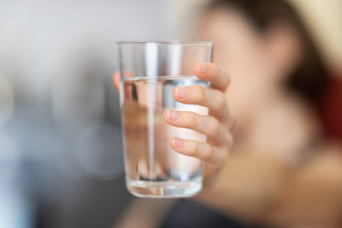 Drinking water: A woman holds out a glass of water against a blurred background